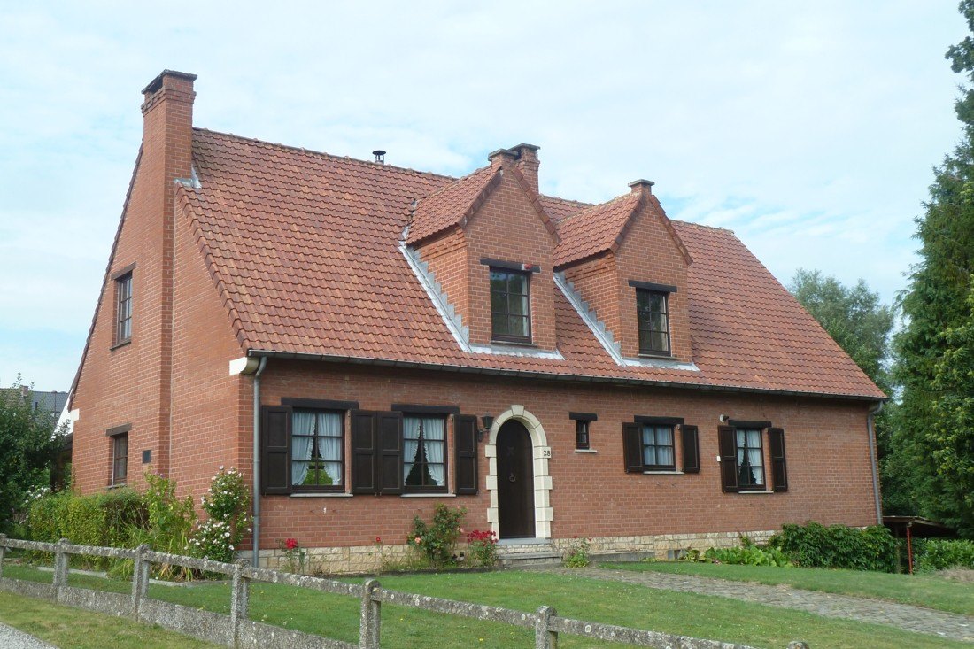 Bakstenen landhuis met twee dakkapellen, luiken en een gebogen voordeur