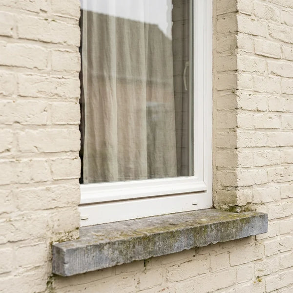 Raam met witte kozijnen en een dikke stenen dorpel in een gevel van crèmekleurige baksteen